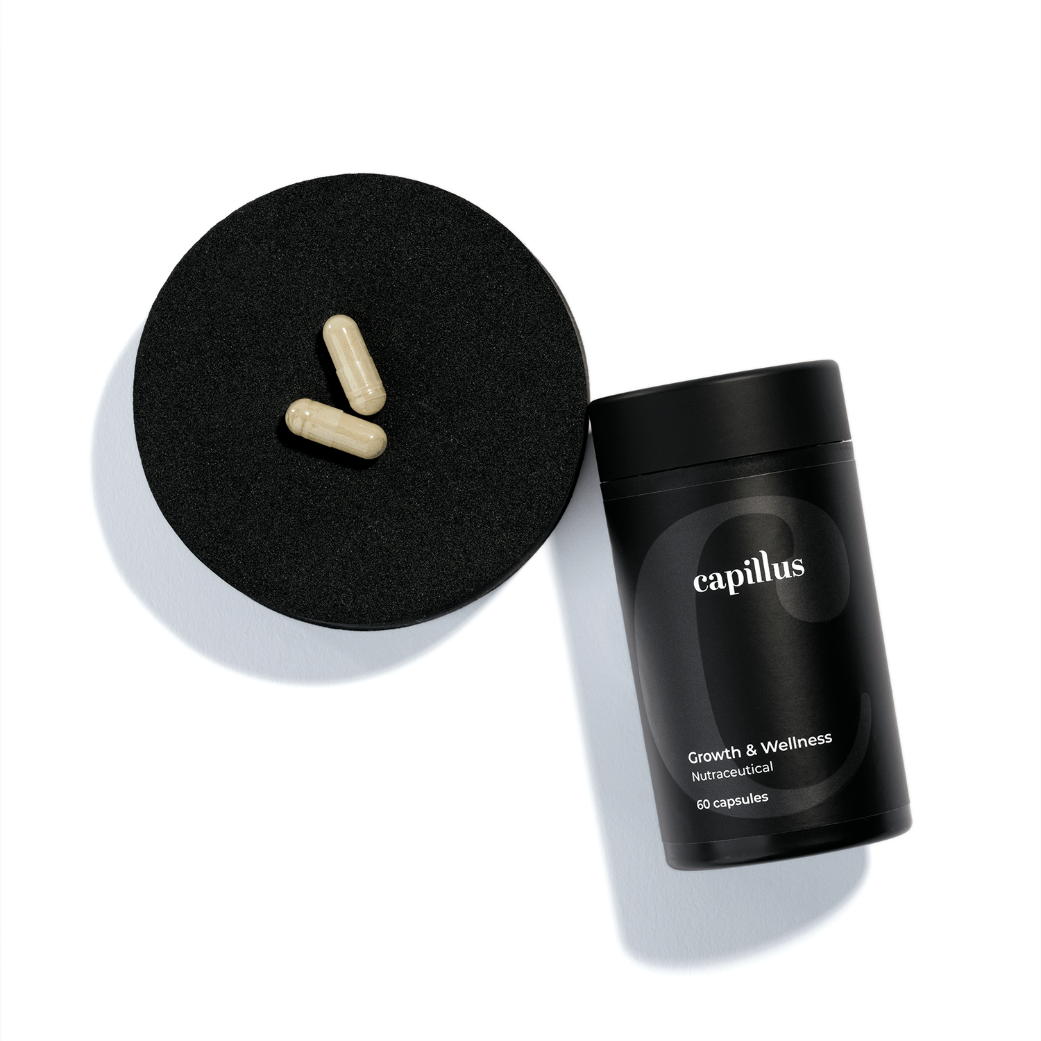 A black container labeled capillus Growth & Wellness Nutraceutical 60 capsules lies next to its lid, with three beige capsules resting on the lid against a white background.