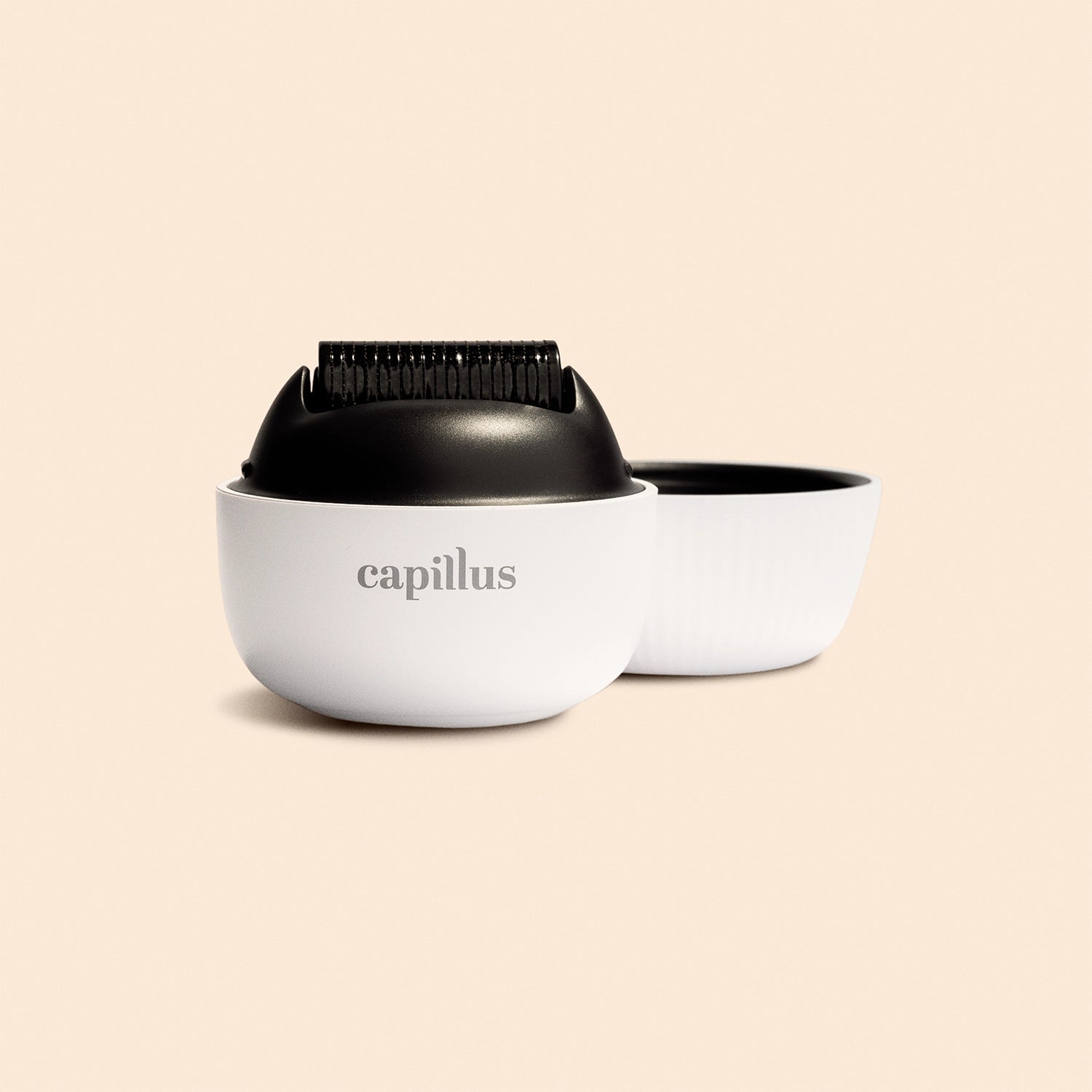A white round Capillus container holds the Capillus Derma Roller, a black device with small teeth. The matching white lid is next to it, all set on a light beige background—ideal for scalp care and hair regrowth routines.