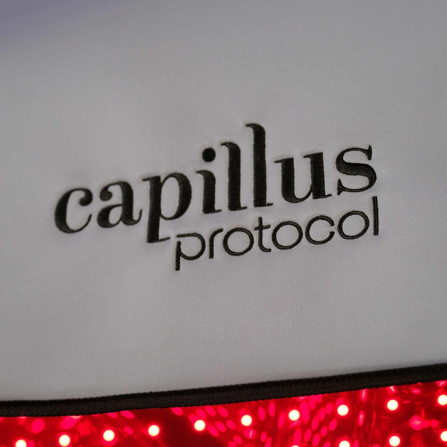 Close-up of the Capillus Healing Pod by Capillus, a white fabric device with glowing red LEDs—highlighting red light therapy technology designed to support muscle recovery and relieve joint pain.
