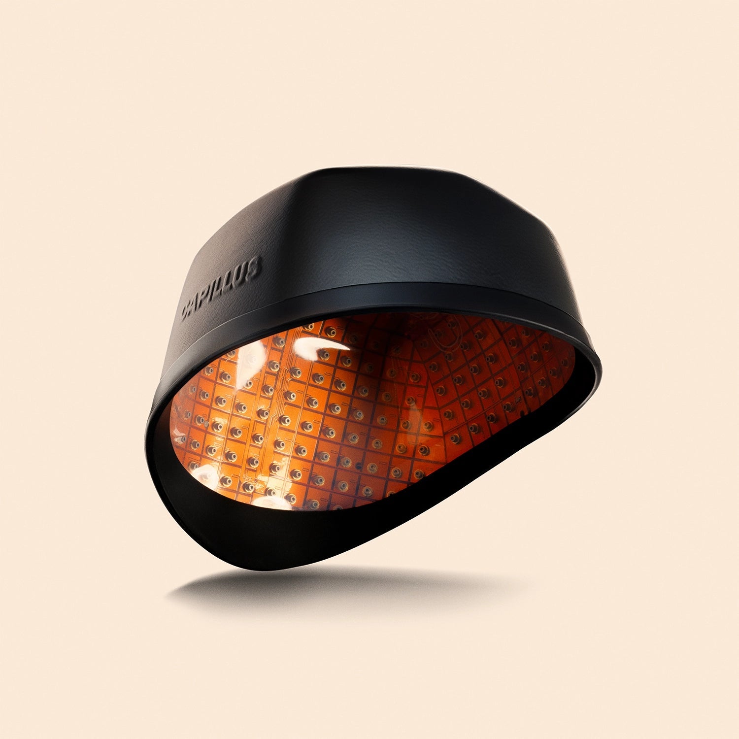 Le Capillus Neuro de Capillus, un casque noir destiné à favoriser la pousse des cheveux et doté d'un panneau LED orange pour la thérapie par lumière rouge et proche infrarouge, est présenté sur un fond beige uni.