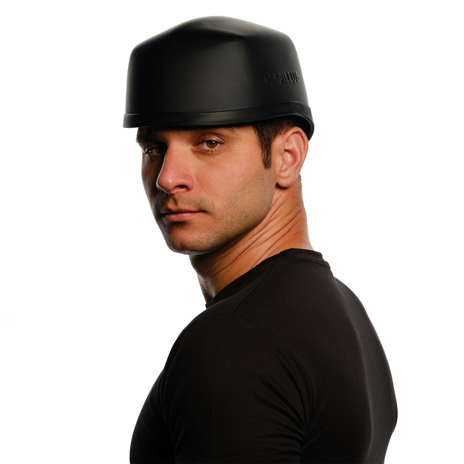 Un homme portant un casque noir et un t-shirt regarde par-dessus son épaule sur un fond blanc, illustrant comment le Capillus Neuro de Capillus utilise la luminothérapie rouge et proche infrarouge pour favoriser les performances cognitives.