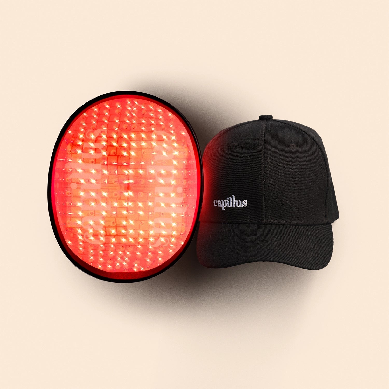 Le Capillus Spectrum de Smart Cap, un appareil rond à LED rouges destiné à favoriser la repousse des cheveux, est présenté à côté d'un bonnet noir pour la repousse des cheveux sur lequel est brodé le mot « capillus » en blanc, sur fond beige.