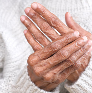 Close-up of an elderly persons hands clasped together, showing wrinkles and textured skin. The person is wearing a light-colored, knitted sweater.