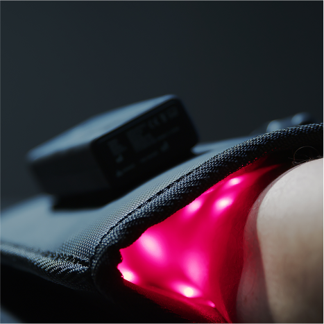 A close-up of a black fabric pouch emitting bright pink light, partially wrapped around a persons arm, with a small digital device attached on top.