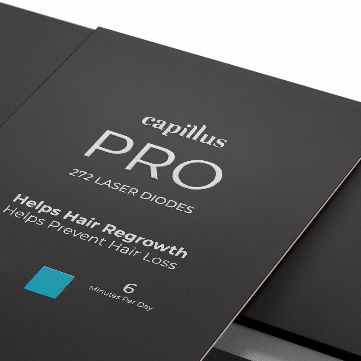 Gros plan sur un emballage du produit Capillus PRO sur lequel figurent les mentions suivantes : « capillus PRO 272 DIODES LASER », « Favorise la repousse des cheveux », « Aide à prévenir la chute des cheveux » et « 6 minutes par jour », à côté d'un carré bleu.