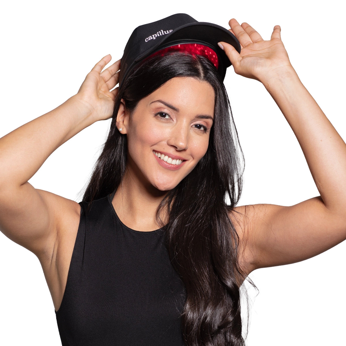 Une femme souriante aux longs cheveux bruns porte un haut noir sans manches et soulève une casquette noire dans laquelle on aperçoit des lumières rouges. Elle tient le bord de la casquette à deux mains.