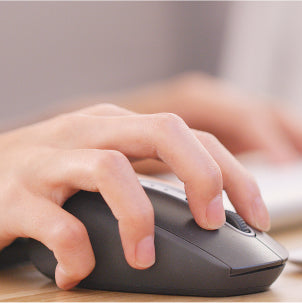A close-up of a persons hand using a black computer mouse, with fingers resting on the buttons, and a keyboard blurred in the background.