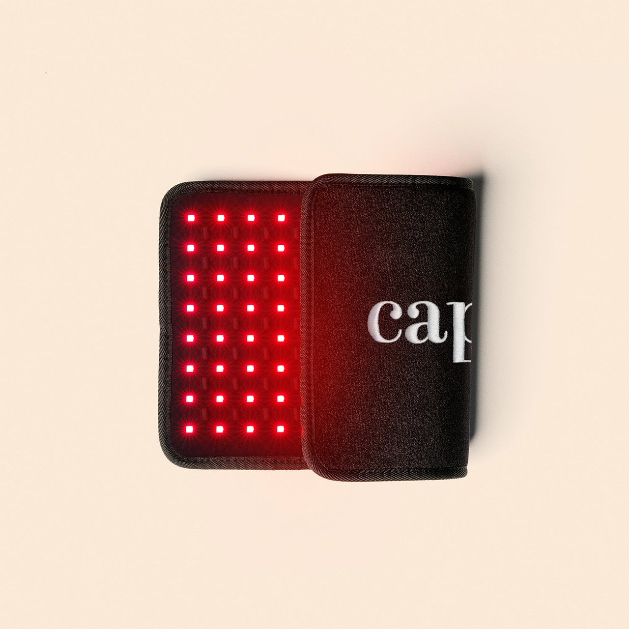 A black rectangular Capillus Body device by Capillus with a grid of small red LED lights for red light therapy, featuring partial white 