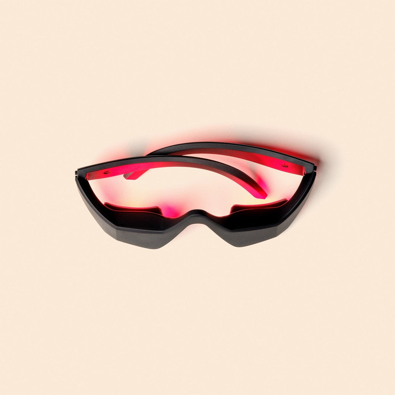 The Capillus EyeLift by Capillus is a pair of futuristic black glasses with red-tinted lenses, inspired by Red Light Therapy to help reduce puffiness, shown against a plain beige background with a faint red shadow beneath.