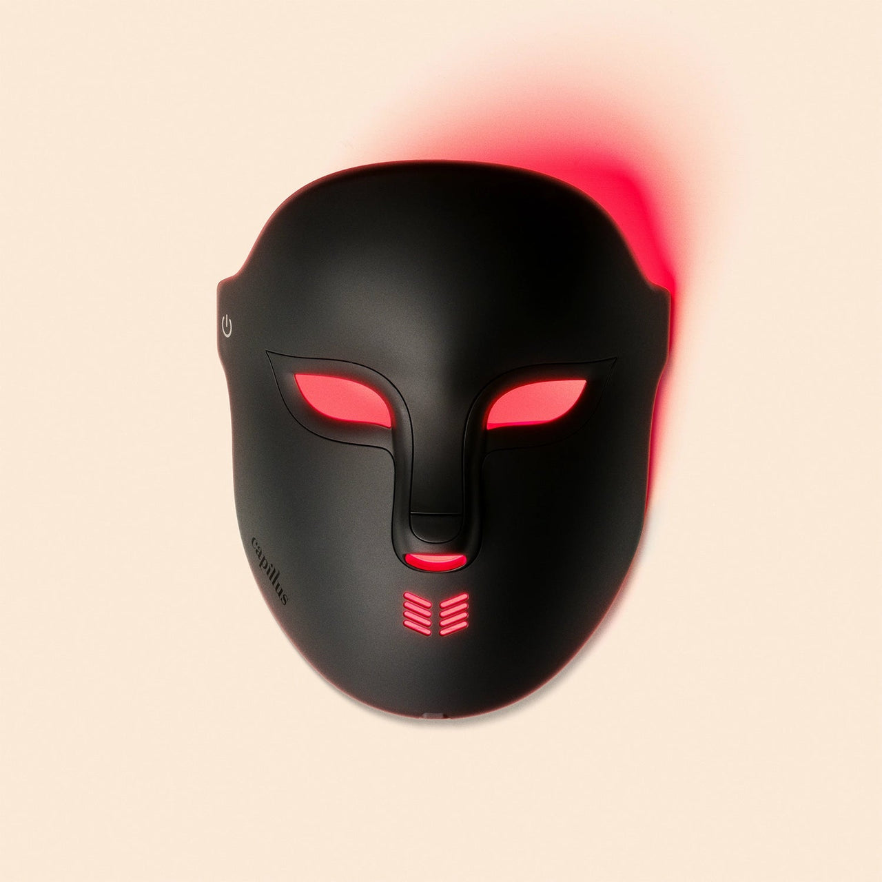 The Capillus Face Mask by Capillus is a black, futuristic LED mask with glowing red lights around the eyes, mouth, and edges, set on a pale beige background. Powered on, it's ideal for light therapy and skin rejuvenation.
