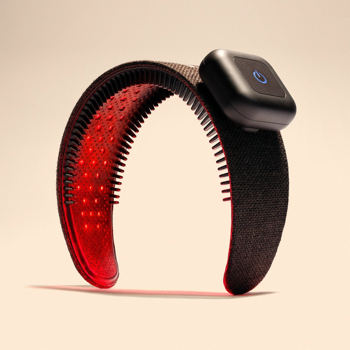The Capillus HairBand by Capillus is a black hair wellness wearable device featuring a rectangular power button. It emits red light from its inner side using medical-grade laser technology, likely intended for therapeutic or health purposes, and is depicted standing upright against a beige background.