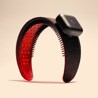 The Capillus HairBand by Capillus is a black hair wellness wearable device featuring a rectangular power button. It emits red light from its inner side using medical-grade laser technology, likely intended for therapeutic or health purposes, and is depicted standing upright against a beige background.