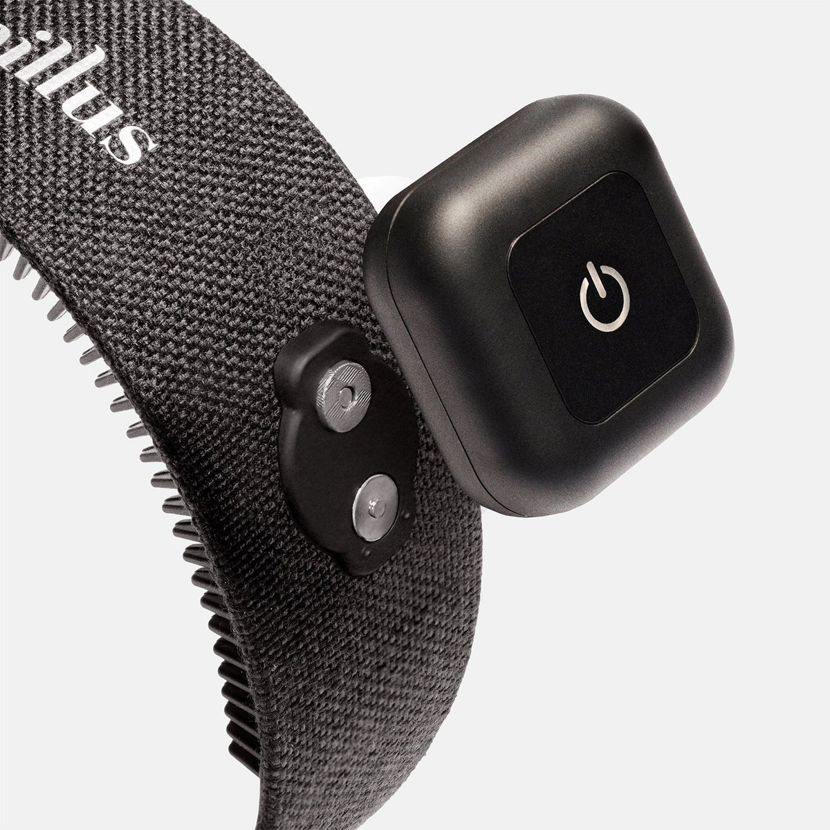 A close-up of a gray textured strap with metal prongs and a black electronic device featuring a power button, both attached to the strap—this innovative hair wellness wearable is the Capillus HairBand by Capillus, designed with medical-grade laser technology.