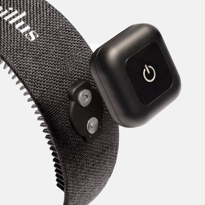 A close-up of a gray textured strap with metal prongs and a black electronic device featuring a power button, both attached to the strap—this innovative hair wellness wearable is the Capillus HairBand by Capillus, designed with medical-grade laser technology.