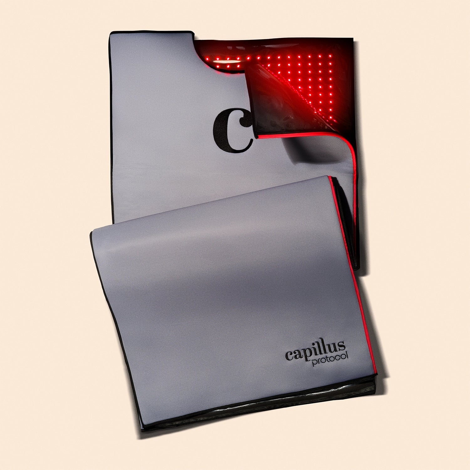 A gray Capillus Healing Pod by Capillus is folded open to display its inner red LED lights for red light therapy and hair treatment, set against a neutral background.