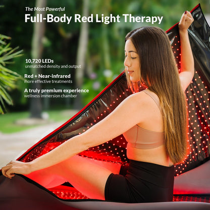 Une femme est assise à l'intérieur d'une capsule de soins Capillus rouge, ouverte et portable, dont l'intérieur est tapissé de nombreuses petites LED utilisées pour la luminothérapie par infrarouge proche.