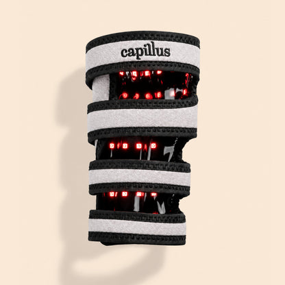 The Capillus Pet Joint Wrap—a wearable device with gray and black bands—emits red LED lights, utilizing near-infrared light therapy designed for joint health in pets, displayed on a beige background.