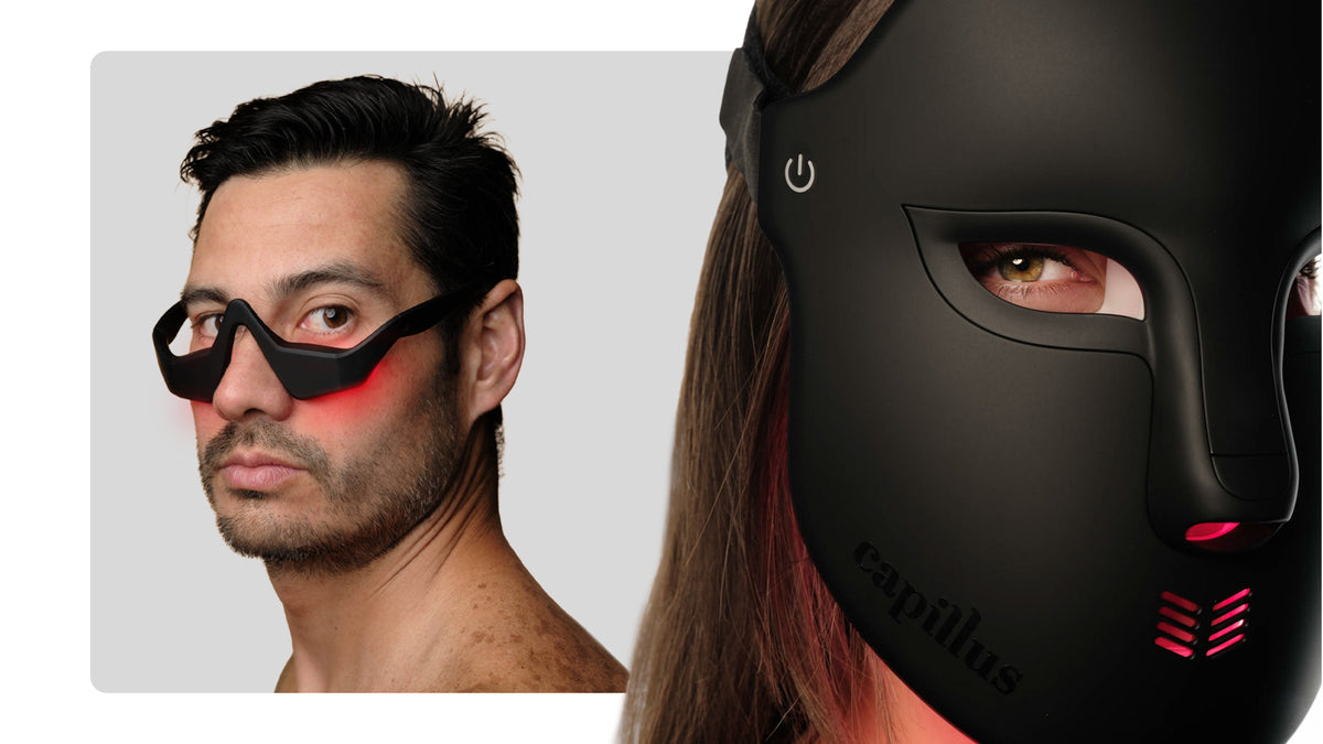 Two people wear black high-tech devices: on the left, a man with a lighted mask over his cheeks and nose; on the right, a woman wears a full-face mask labeled “capillus” with red lights glowing.